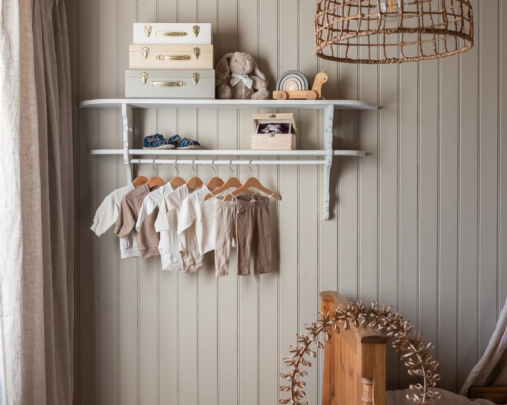 En vägg med träpanelen pärlspont och en hylla med barnkläder och dekorationer, samt andra inredningsdetaljer