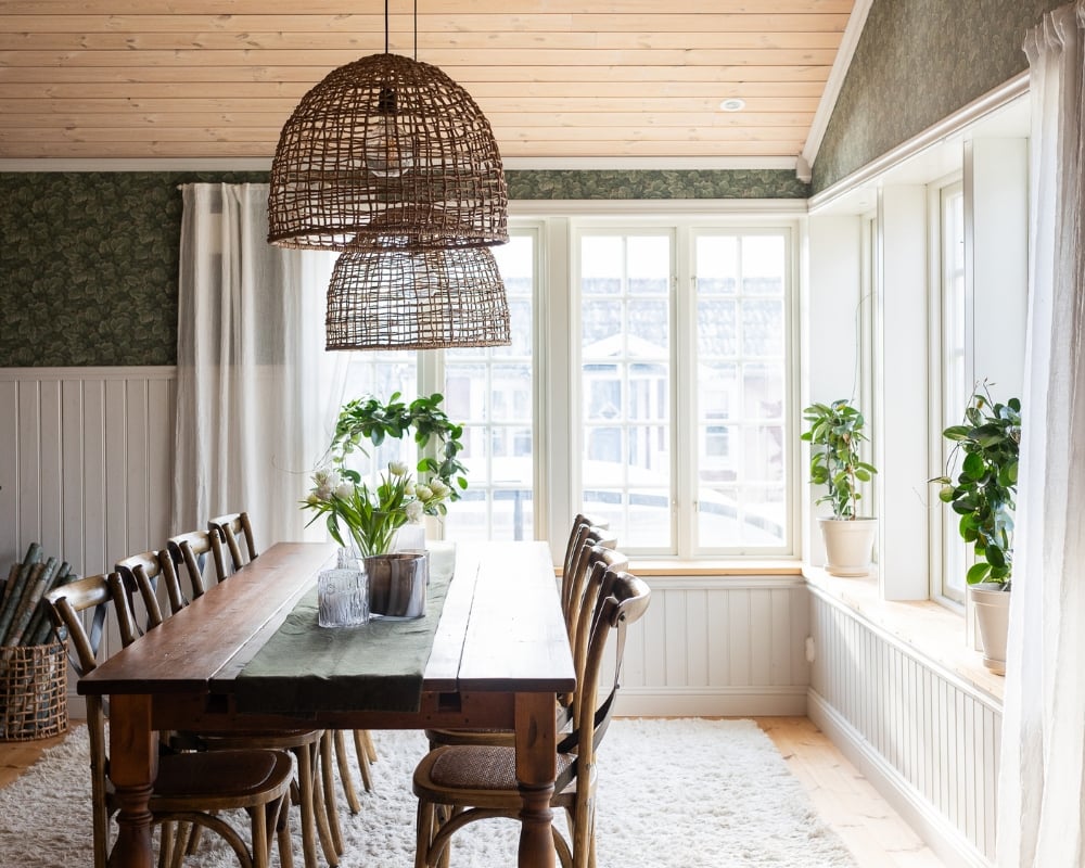 Ett rum med matbord och stolar i trä, bröstpanel i vitt, trägolv och trätak, samt inredning