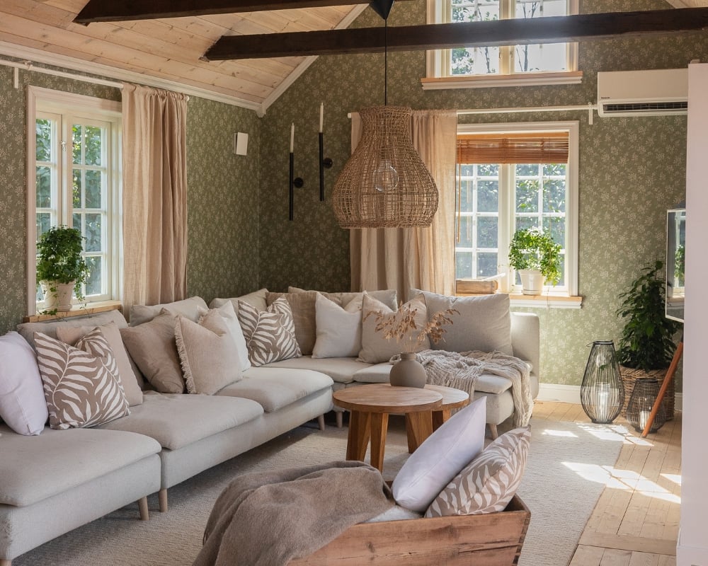 Ett vardagsrum med soffa, kuddar och filtar, samt övriga dekorationer. Träbalkar i taket, samt trägolv och trätak