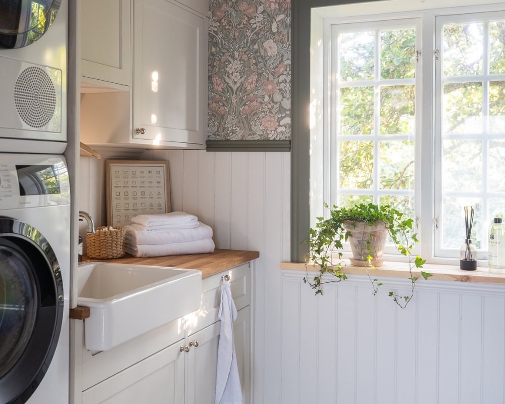 En tvättstuga med vit bröstpanel och handfat med vita luckor över och under