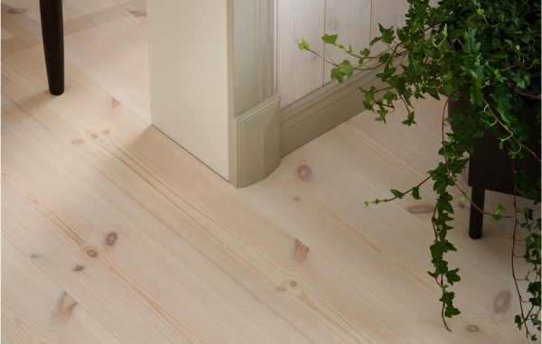Ljust trägolv med vägg som har ljusa lister och dekorkloss. Samt även en stol och grön växt