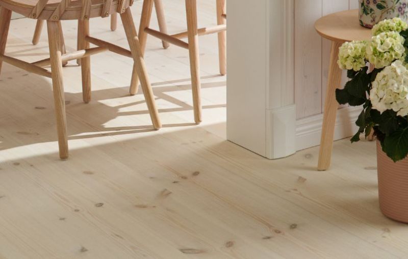 Ett massivt furugolv där man ser matplatsens stolsben och en kruka med en hortensia som står på golve