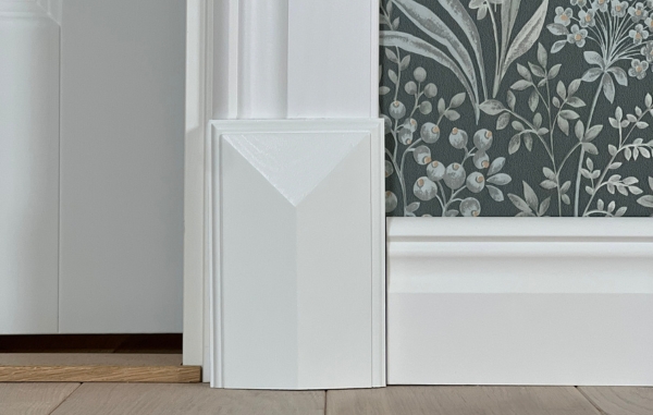 Vita lister och en vit golvkloss, samt en grön tapet med mönster