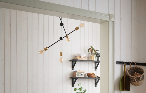 En dörröppning med foder, vit panel och inredning i form av taklampa och hylla på väggen med dekorationer