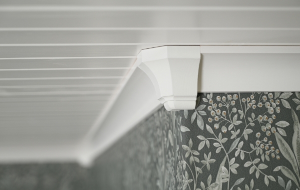 Ett tak med vit panel, vita lister och en vit hörnkloss, samt en grön tapet med mönster