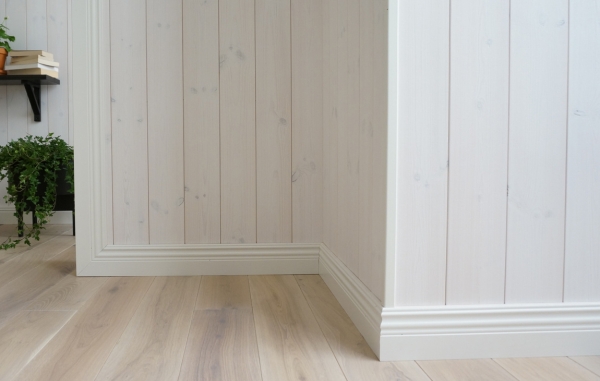 En vägg med panel och vita lister, samt ett trägolv