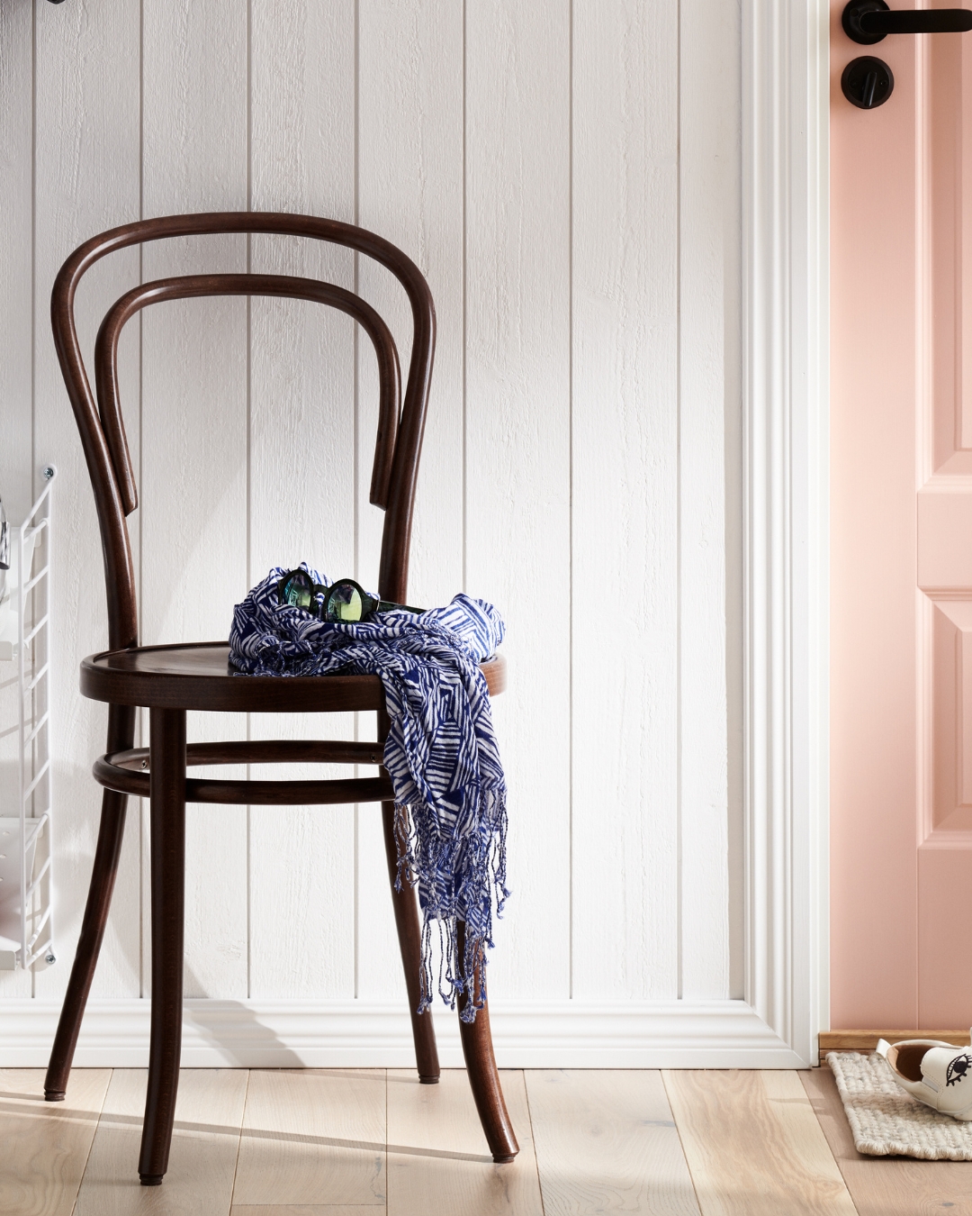 Vit panel och lister, trägolv och en brun stol med ett klädesplagg på