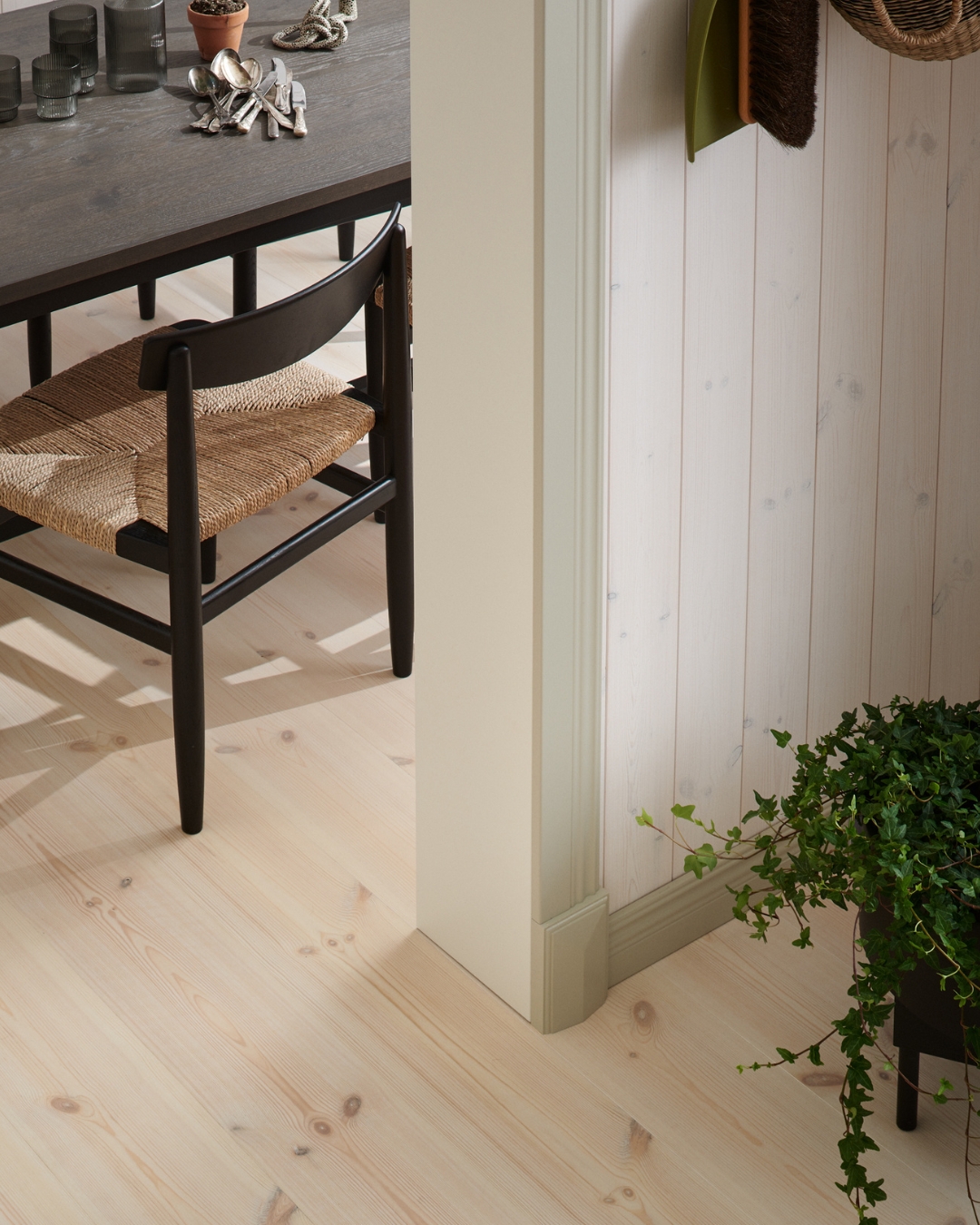 En vägg med vit panel, beiga lister och trägoilv, samt bord och stolar