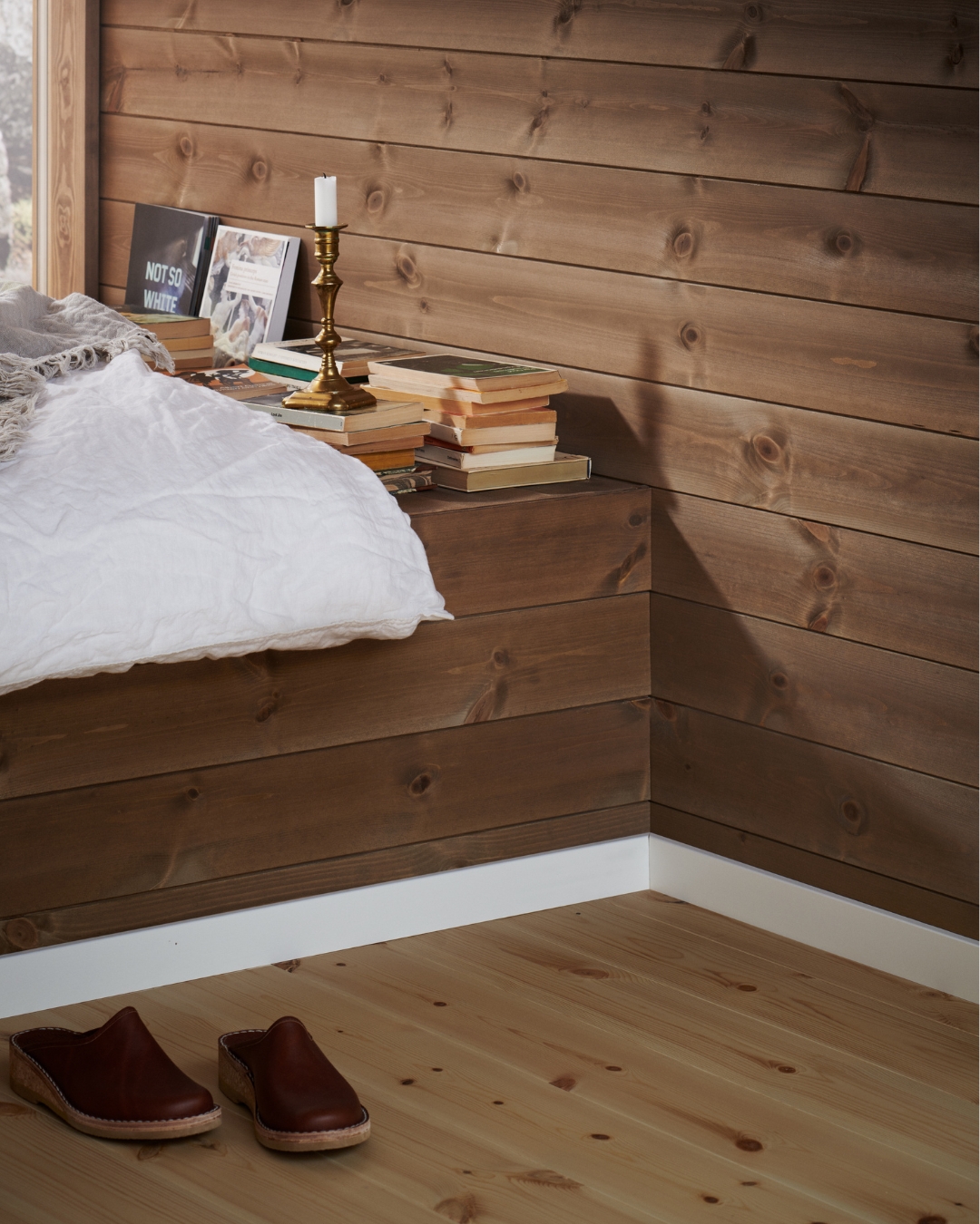 Träpanel, trägolv och vita lister, samt en bänk med vitt täcke