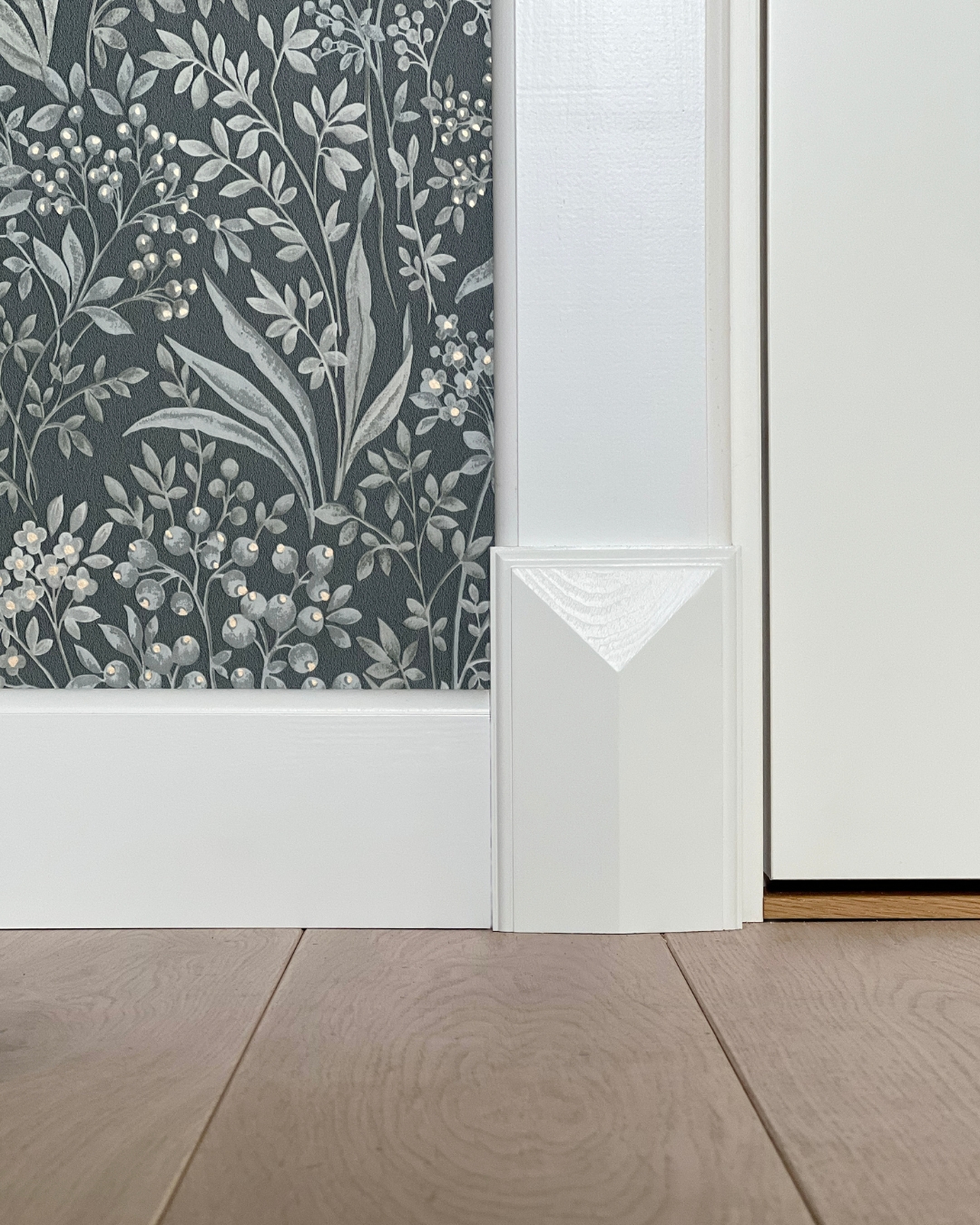 Vägg med vita lister och vit golvkloss, samt grön tapet med mönster