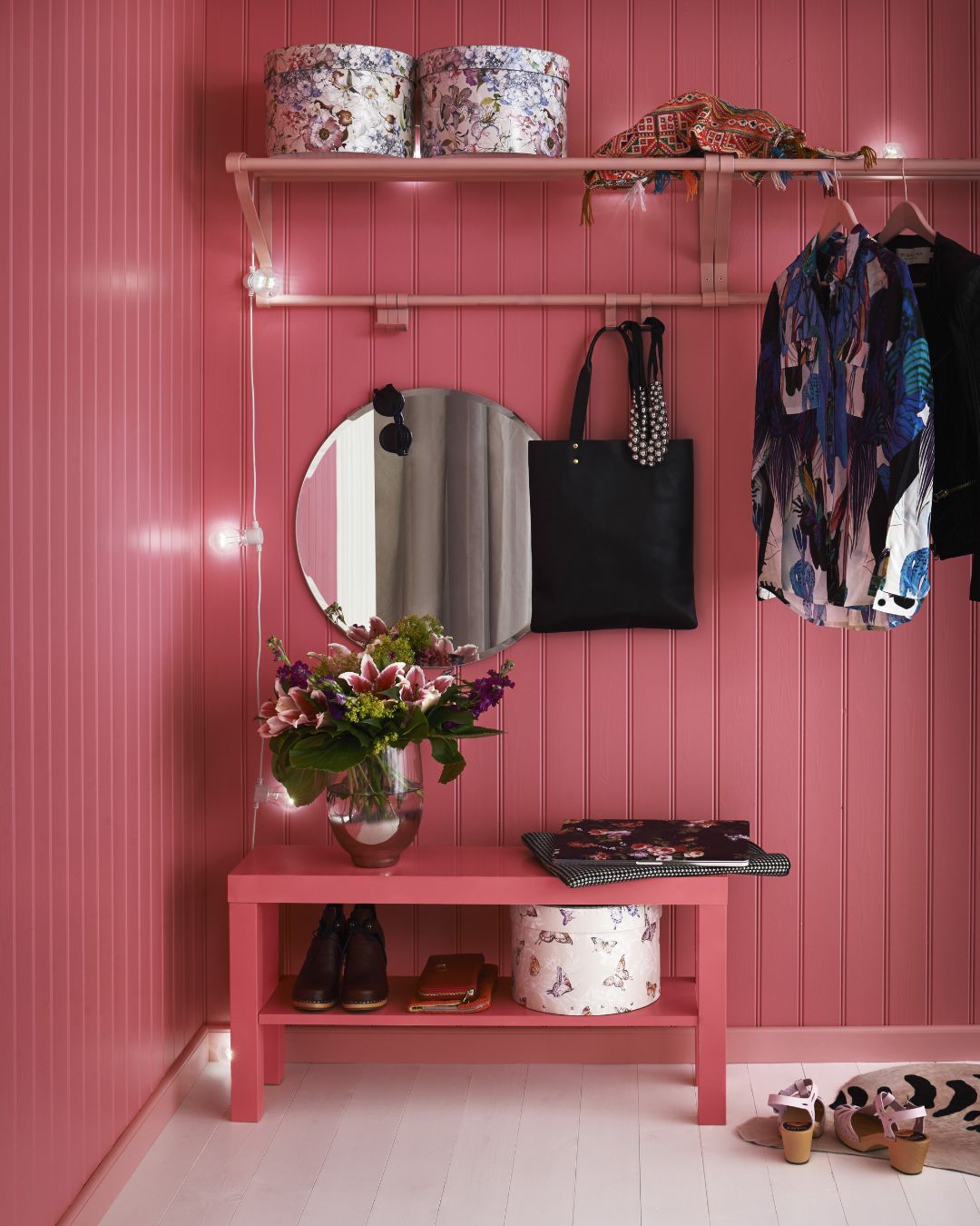 Hall med rosa träpanel på väggarna. Kläder hänger på hatthyllan och två boxar står överst.