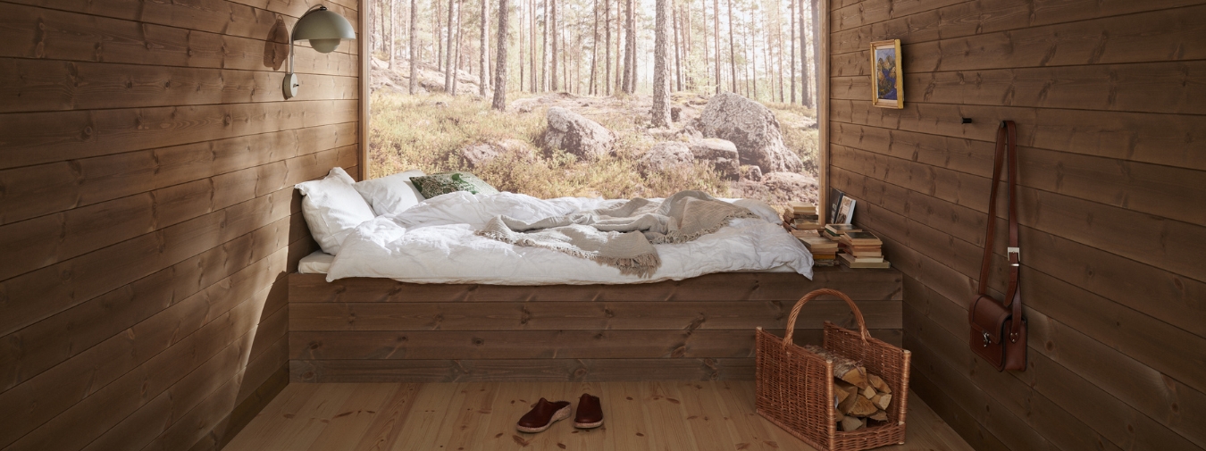 Träpanelen Stilla Skogsbrun sitter på väggarna och i taket. Rakt fram ett stort fönster med utsikt mot en tallskog. Fönstret täcker hela väggen.