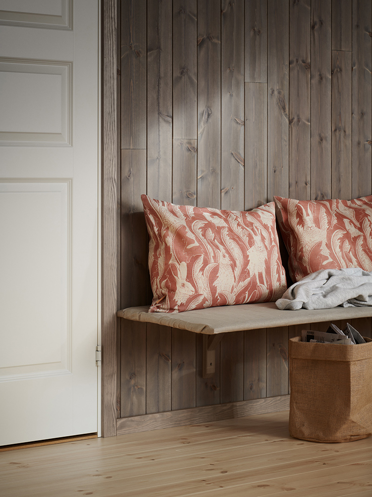 Träpanelen Stilla Gärdsgårdsgrå på väggen och färganpassad golvlist och foder. Kuddar ligger på en platsbyggd bänk.