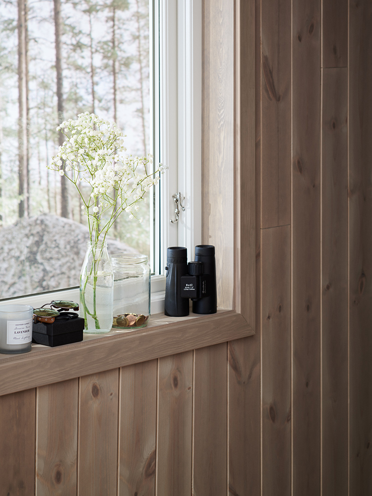 Träpanelen Stilla Sandbeige sitter på väggarna i ett sovrum med utsikt över tallskogen.
