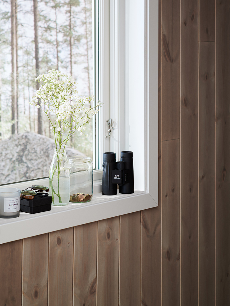 Träpanelen Stilla Sandbeige sitter på väggarna i ett sovrum med utsikt över tallskogen.