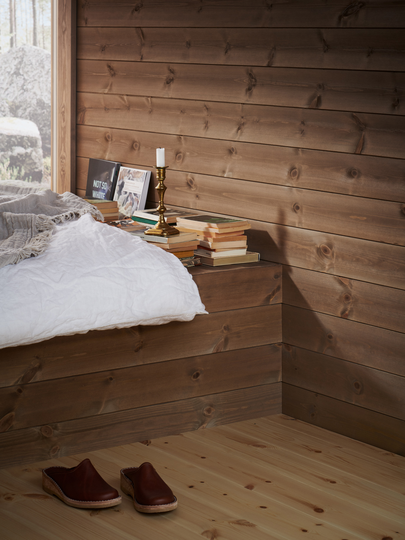 Träpanelen Stilla Skogsbrun sitter på väggarna. Rakt fram ett stort fönster med utsikt mot en tallskog.