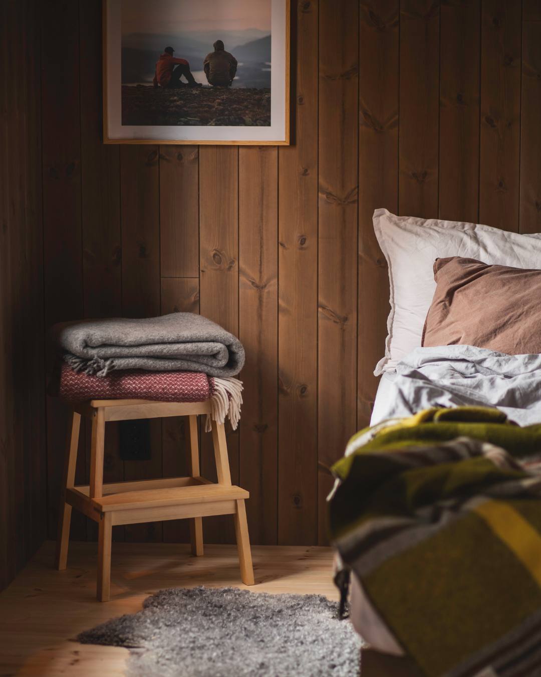 Soverom med mørkebrunt stående panel, en enkel krakk med ulltepper og en delikat seng.