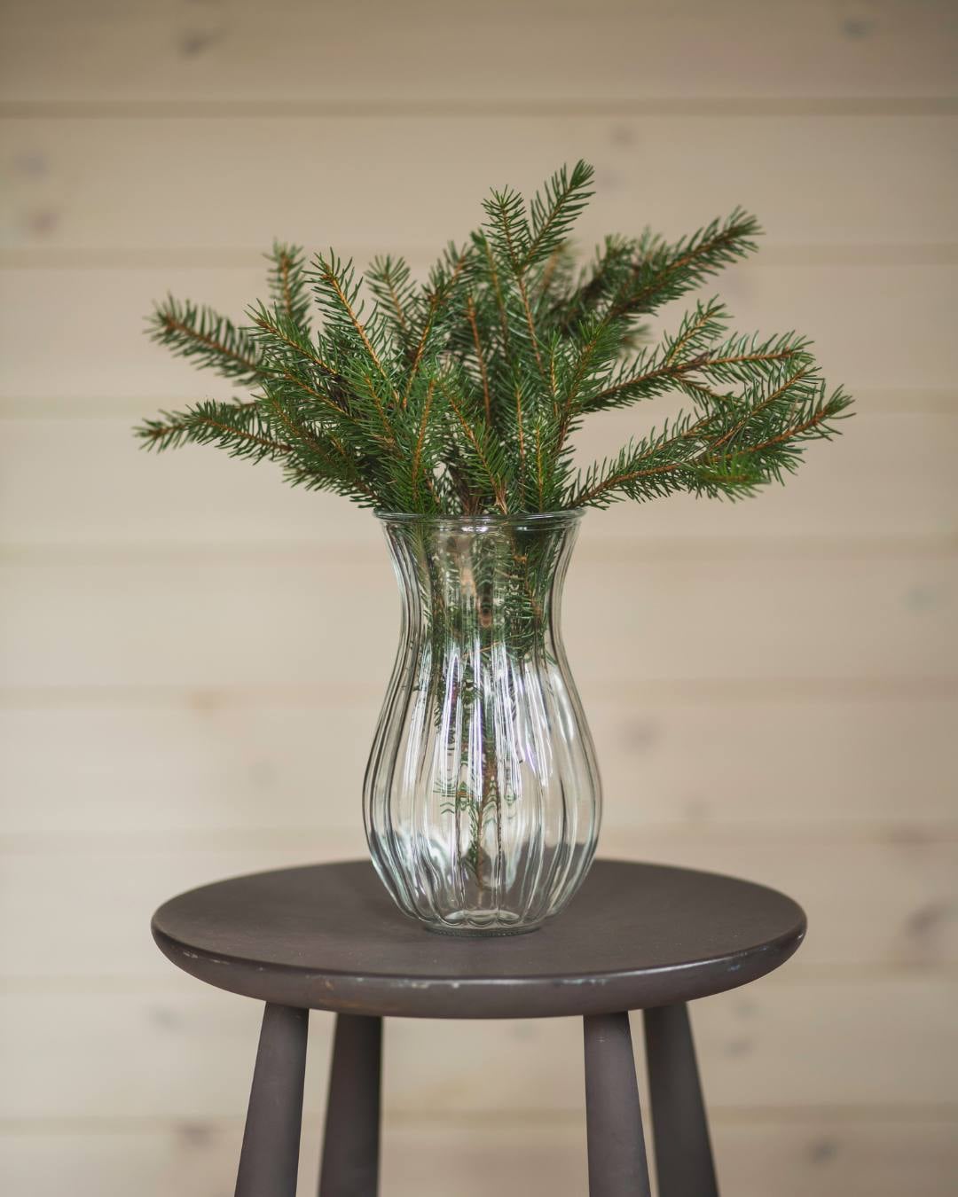 Krakk med vase som inneholder granbar. Alt er plassert foran lysbeiset liggende panelvegg