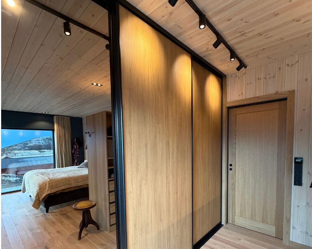 Soverom på Haveng med lyst trepanel på vegg og i tak, eikegulv, garderobe og store vindusflater mot naturen.