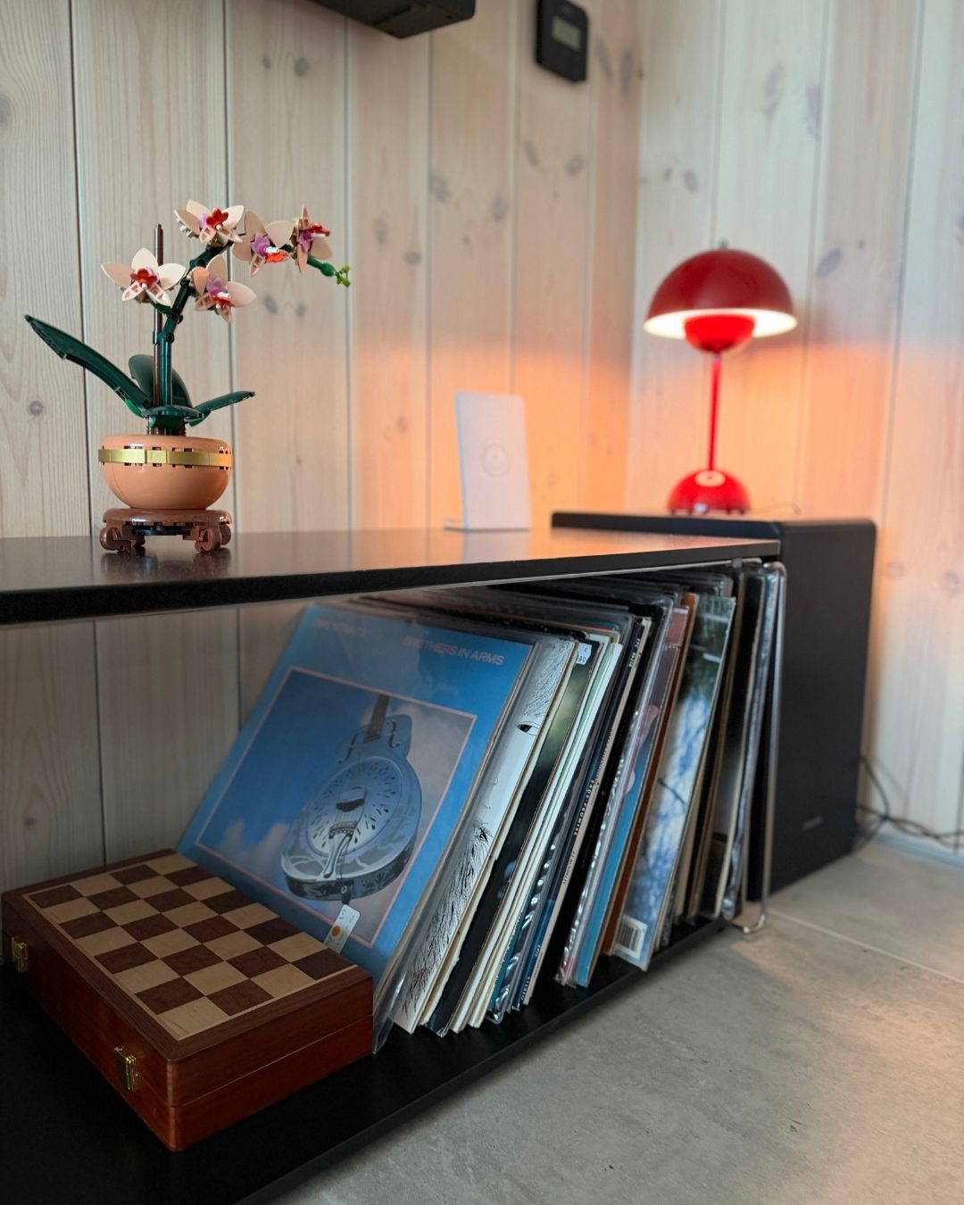 Platesamling, rød bordlampe og dekor foran en vegg med lyst trepanel.
