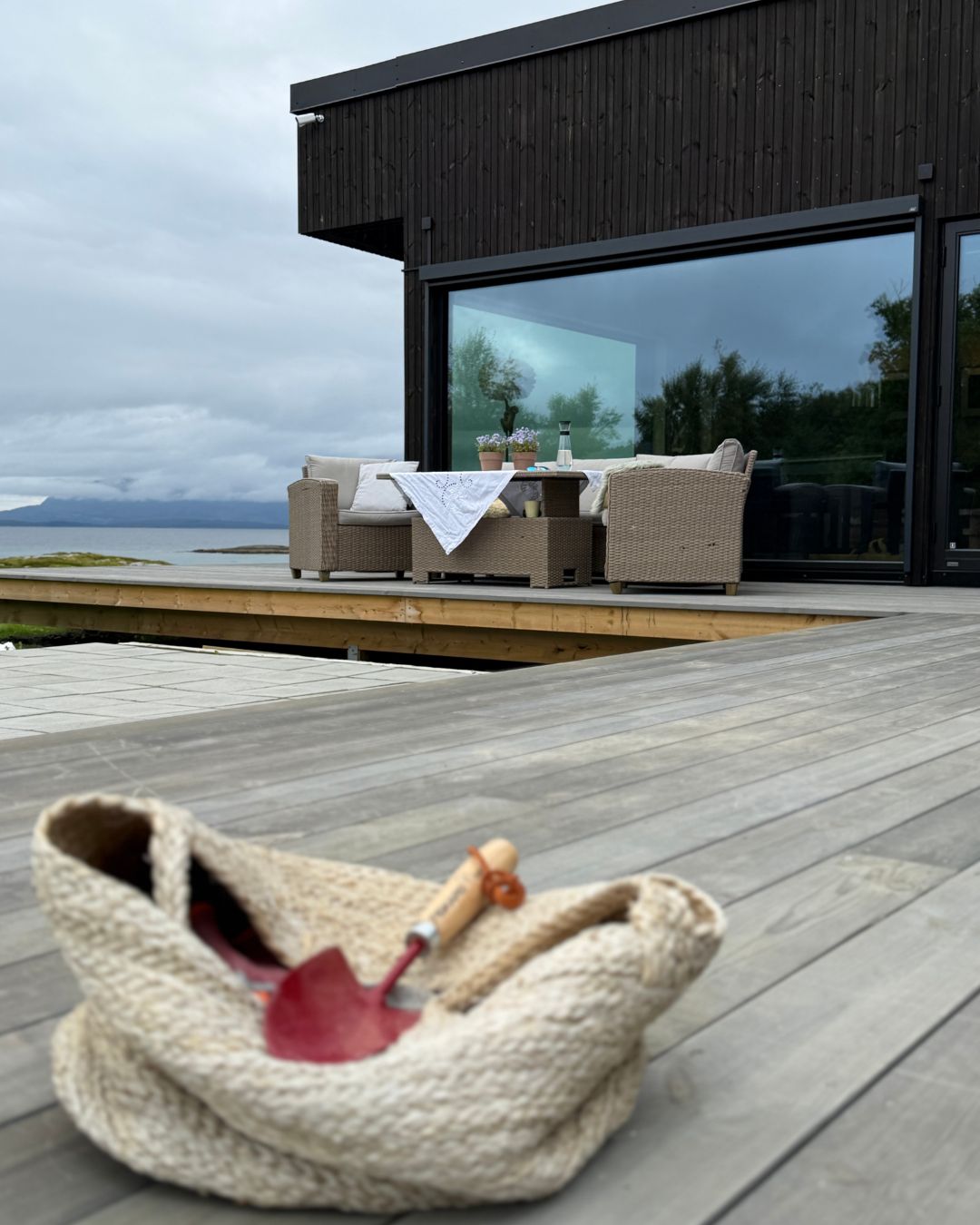 Terrasse med sittegruppe foran den mørke trefasaden på Haveng, med hav og fjell i bakgrunnen.