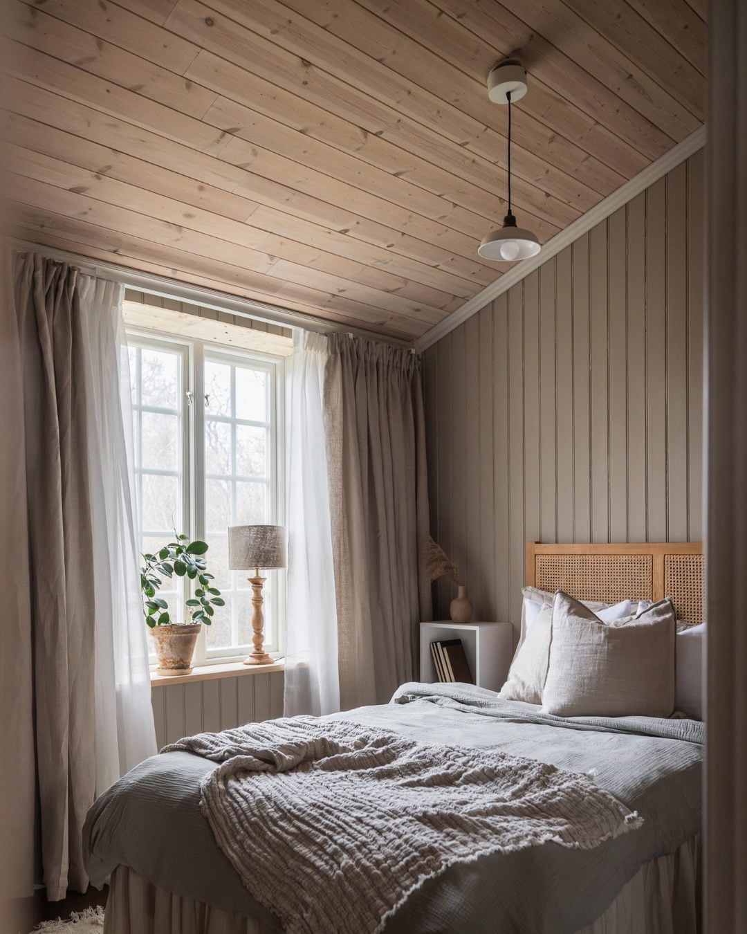 Soverom i beige toner, sengegavel i rotting og stående perlespontpanel på veggene. Hvitlasert trepanel i taket.