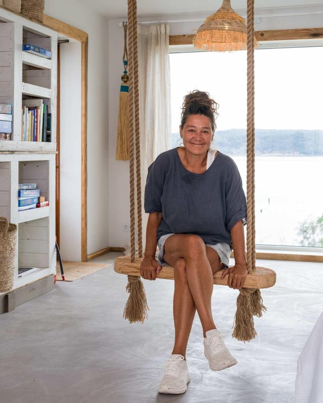 Sonja Lee sitter i en innendørs huske av tau og tre i en lys stue med utsikt over Oslofjorden.