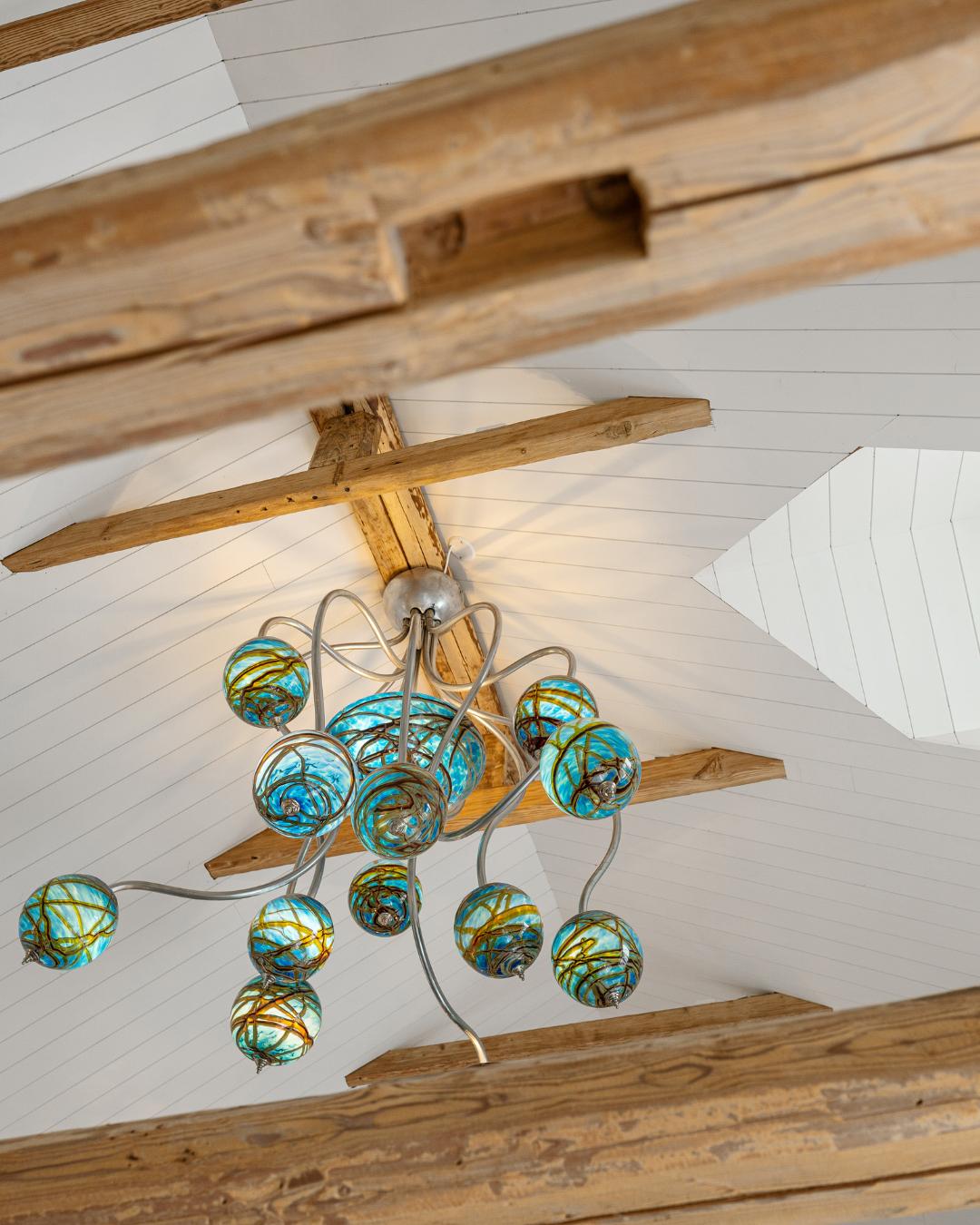 Taklampe med turkise glasskuler henger fra eksponerte trebalker under et hvitt tak kledd med Sprekkpanel i Villa Oslofjord.