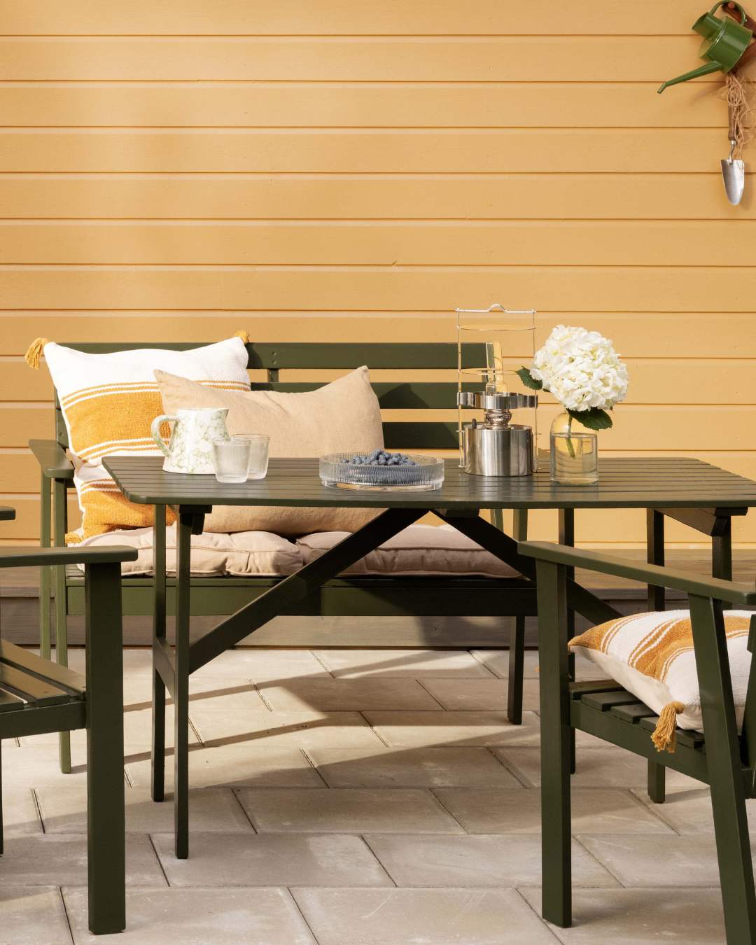 Gul liggende kledningsvegg med grønne hagemøbler foran.