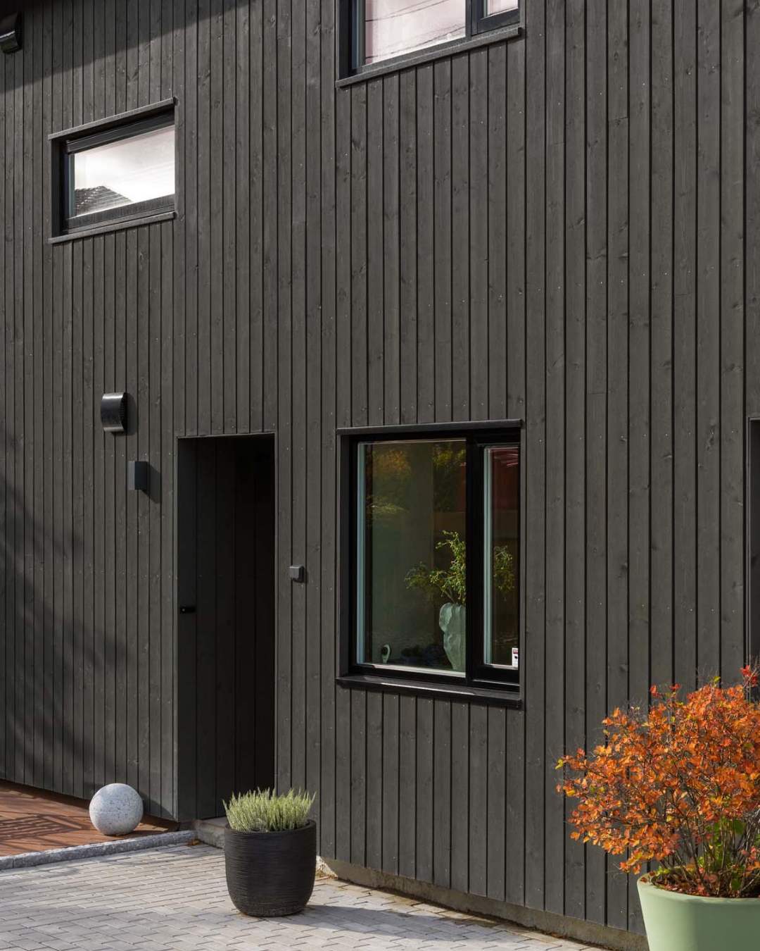 Hus med stående utvendlig kledning i en brunfarge. oransje plante foran.