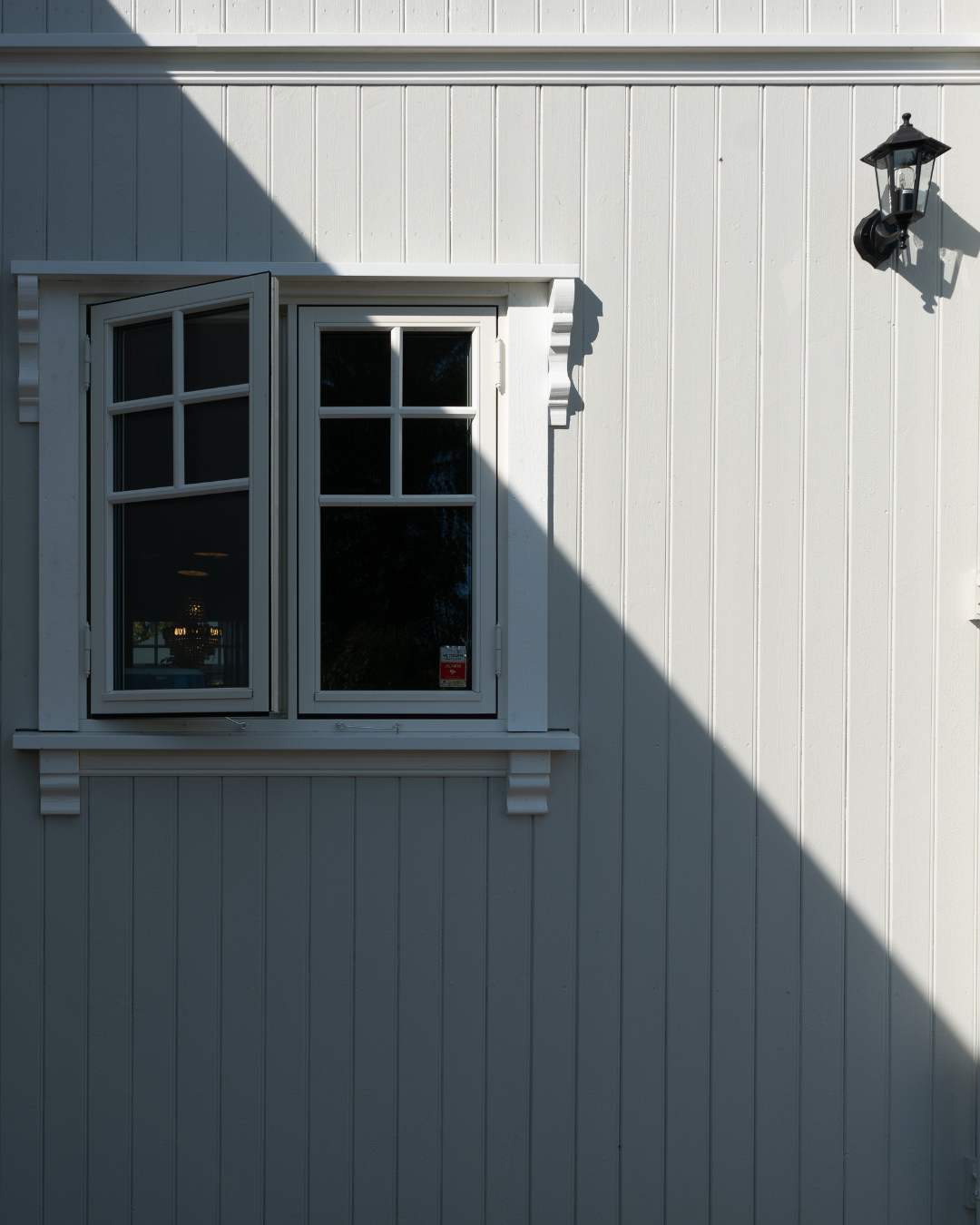 Kledningsvegg med stående kledning og et vindu. Kledningen er grå-hvit