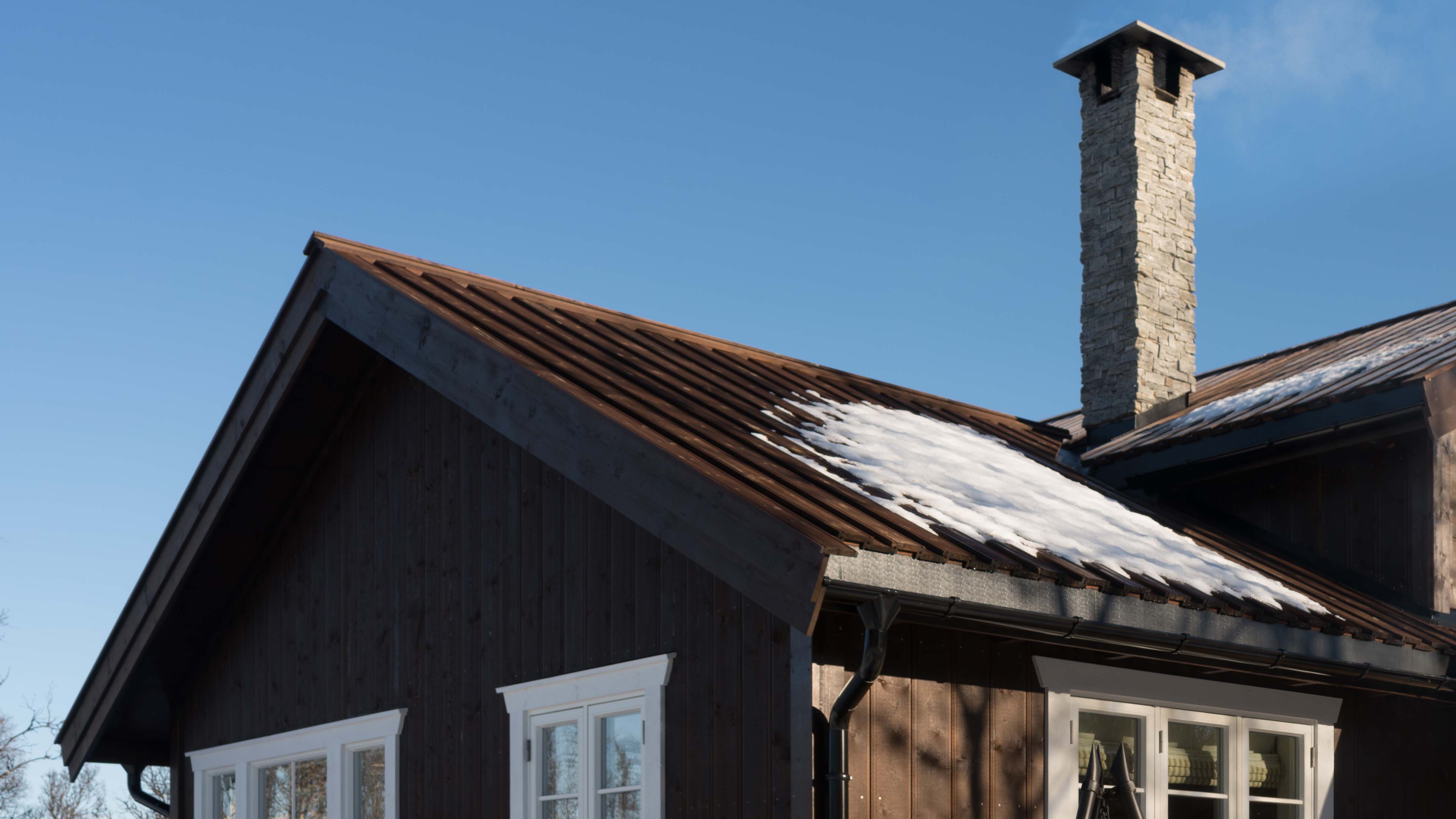 Brunbeiset hytte med tretak med svarte takrenner og takrennekroker.