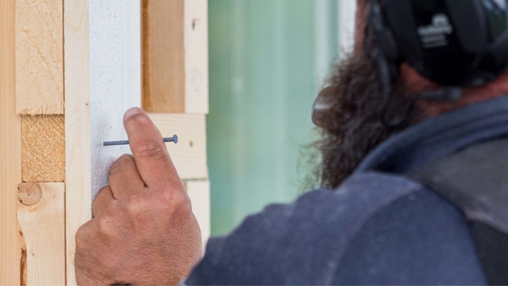 Person som slår inn en spiker for å montere kledning på et hus