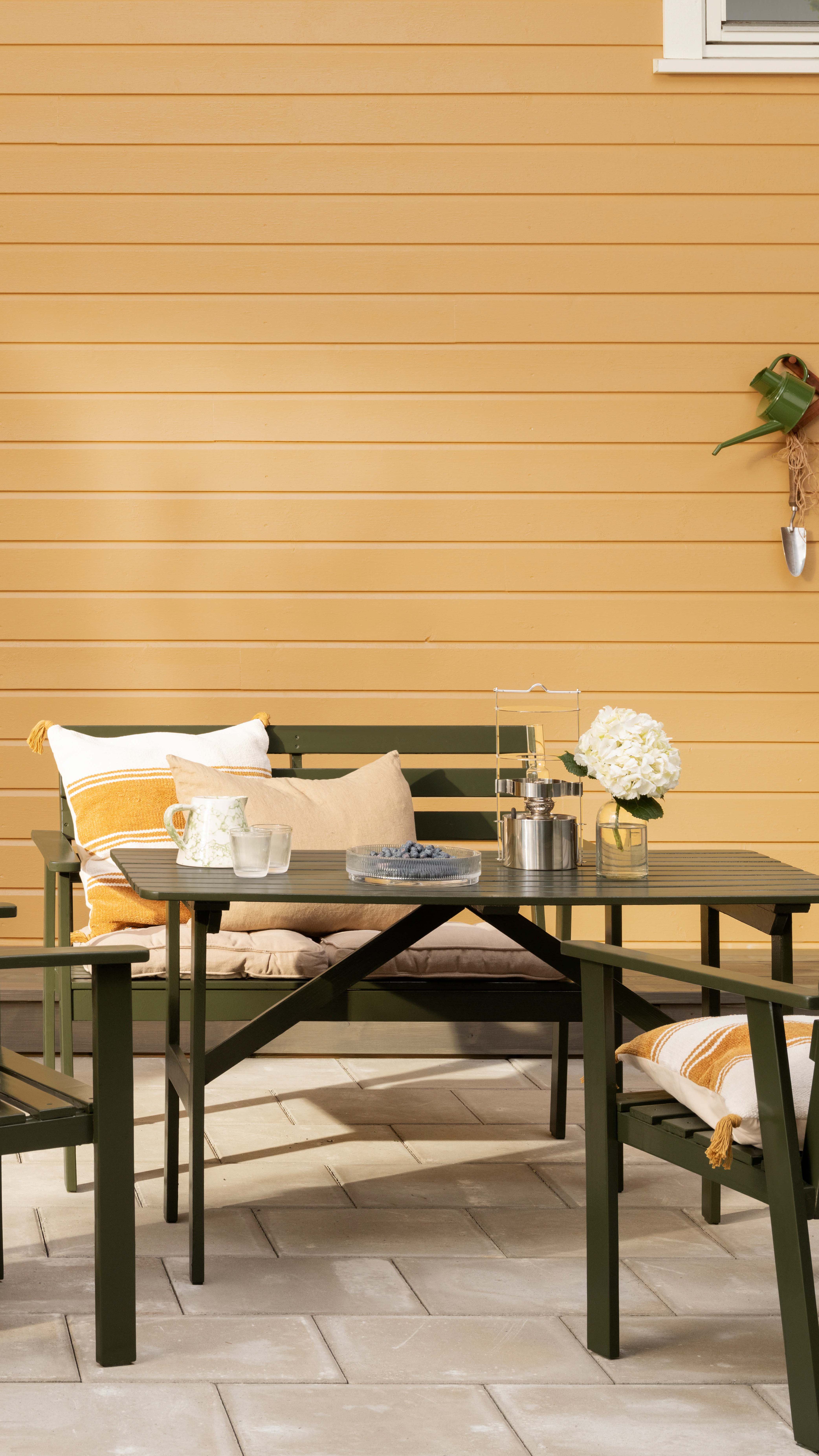 En gul kledningsvegg med terrassemøblement foran.
