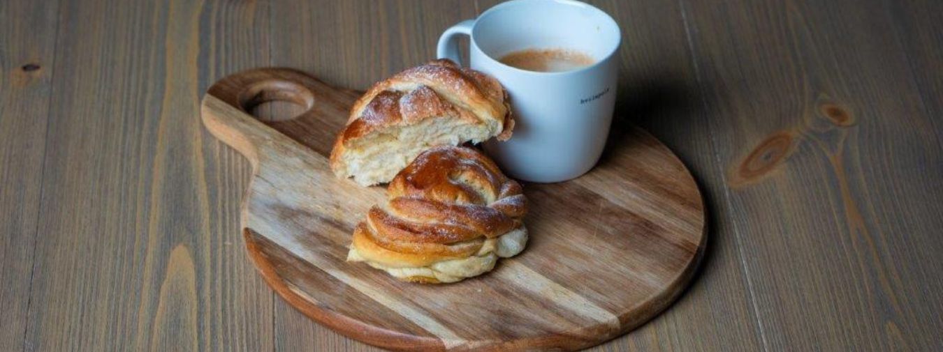 Et trebrett er plassert på gulvet med kanelboller og en kopp med kaffe.