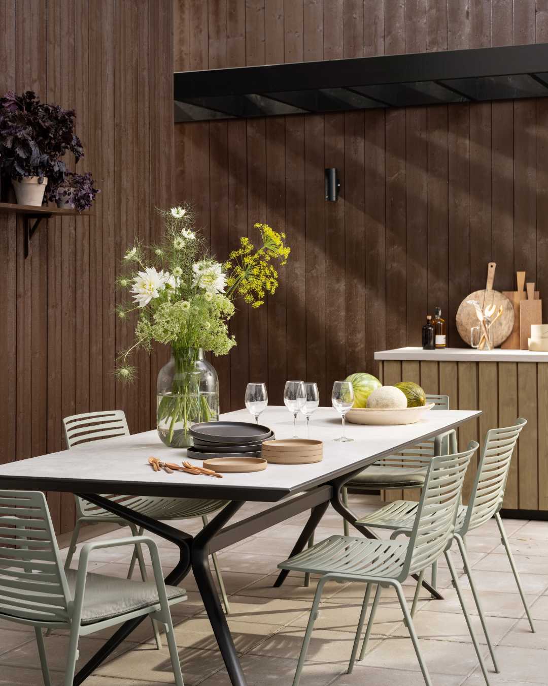 Terrasse med dekket bord fasade i bakgrunnen med stående trekledning besiet brun.