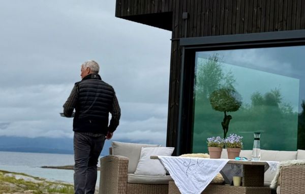 Jan Roger går langs terrassen foran den mørke Værbitt-fasaden på Haveng, med havet i bakgrunnen.
