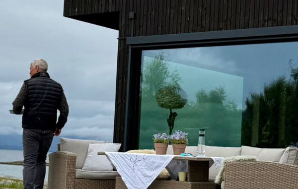 Jan Roger går langs terrassen foran den mørke Værbitt-fasaden på Haveng, med havet i bakgrunnen.