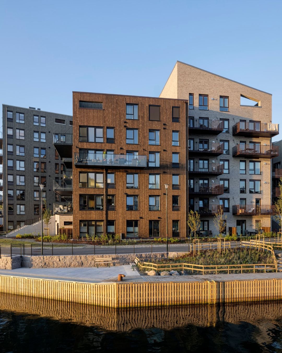 Moderne leilighetsbygg ved vannet med stående Værbitt kledning i fargen Barka.