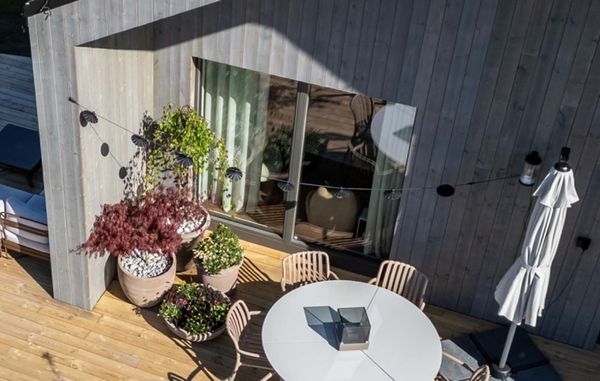 Et grått hus med parasoll, terrasse, planter og møbler