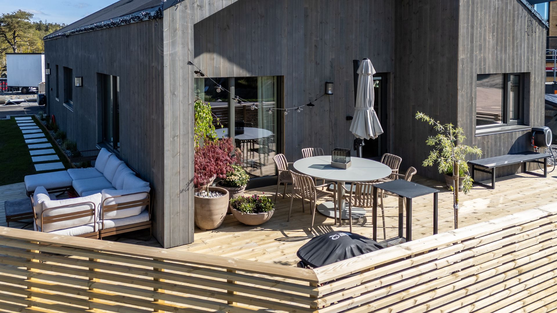 Stor treterrasse rundt moderne bolig med spiseplass, loungeområde, planter og levegger.