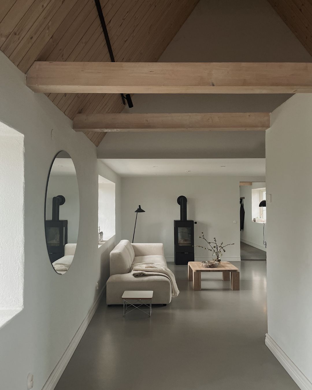 Lyst og mininalistisk møblert hjem med sofa, bord og en svart peis. Tretaket går helt opp i mønet.
