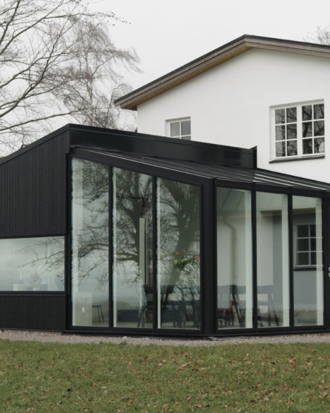 Hvitt stenhus med svart tilbygg med store vinduer