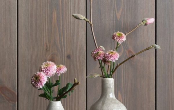 Detaljbilde av mørkbeiset trepanel med synlig trestruktur, dekorert med rosa blomster i keramikkvaser.
