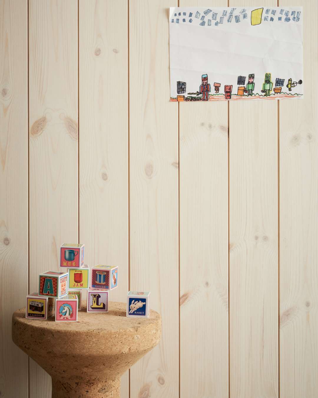 Trepanel Sprekk i hvitlasert bak en liten krakk med treleker oppå. På veggen henger en barnetegning.