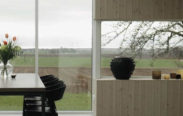 Lys spisestue med naturfarget trepanel på vegg og rundt store vinduer med utsikt over landskapet.