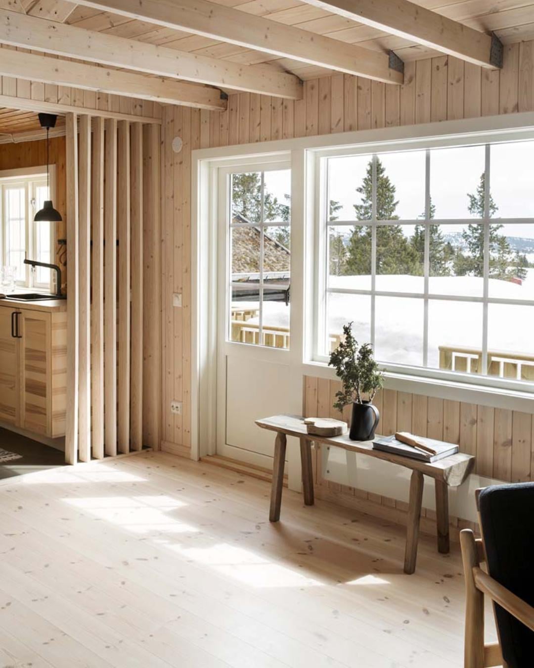 Lys og luftig stue med furugulv, synlige taksperrer og utsikt mot snødekt landskap
